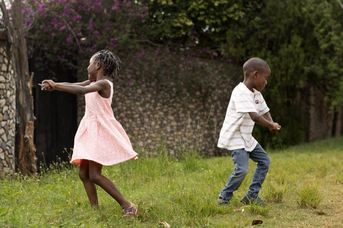 Two children running and playing on grass in a garden